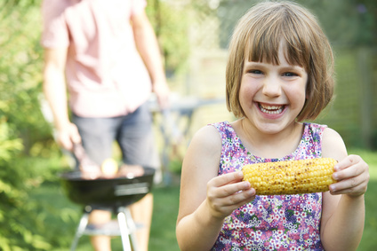 Young Girl Eating Sweetcorn At Family Barbeque